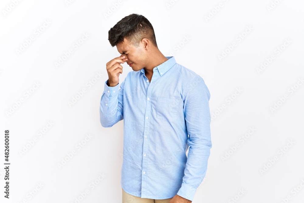 Young hispanic man wearing business shirt standing over isolated background tired rubbing nose and eyes feeling fatigue and headache. stress and frustration concept. Young hispanic man wearing business shirt standing over isolated background tired rubbing nose and eyes feeling fatigue and headache. stress and frustration concept.