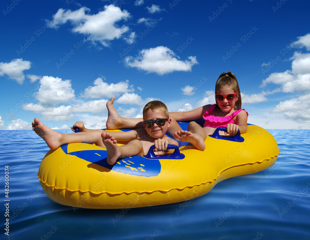 Boy and girl on inflatable float in blue sea water.