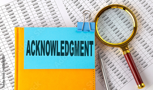 ACKNOWLEDGMENT text on sticker on notebook with magnifier and chart. Business concept