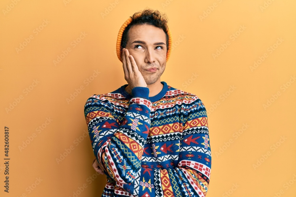 Fototapeta premium Young handsome man wearing wool hat and colorful sweater thinking looking tired and bored with depression problems with crossed arms.