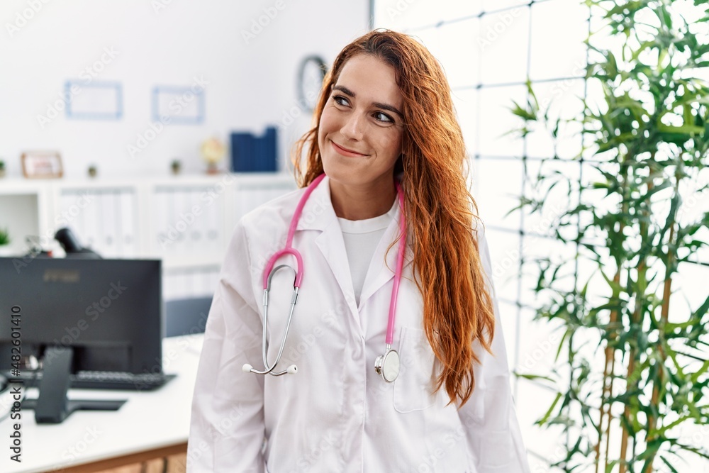 Young redhead woman wearing doctor uniform and stethoscope at the clinic smiling looking to the side and staring away thinking. Young redhead woman wearing doctor uniform and stethoscope at the clinic smiling looking to the side and staring away thinking.