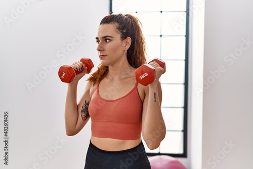 Young redhead woman training with dumbbells at sport center