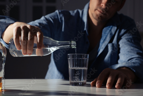 Addicted man with alcoholic drink at table in kitchen, closeup