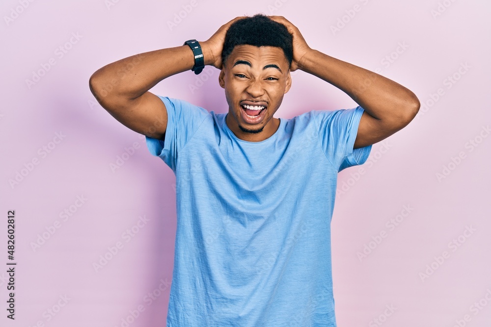 Young african american man wearing casual blue t shirt crazy and scared with hands on head, afraid and surprised of shock with open mouth Young african american man wearing casual blue t shirt crazy and scared with hands on head, afraid and surprised of shock with open mouth
