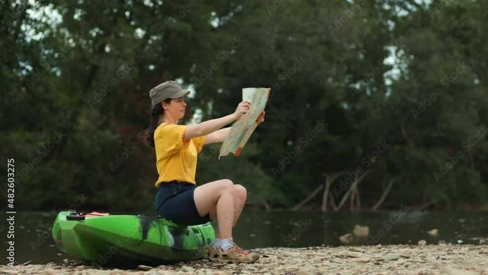 World Tourism Day. A young woman is sitting on a kayak, unfolding a paper map that is crumpled by the wind. Real time. Camping and tourism concept. World Tourism Day. A young woman is sitting on a kayak, unfolding a paper map that is crumpled by the wind. Real time. Camping and tourism concept.