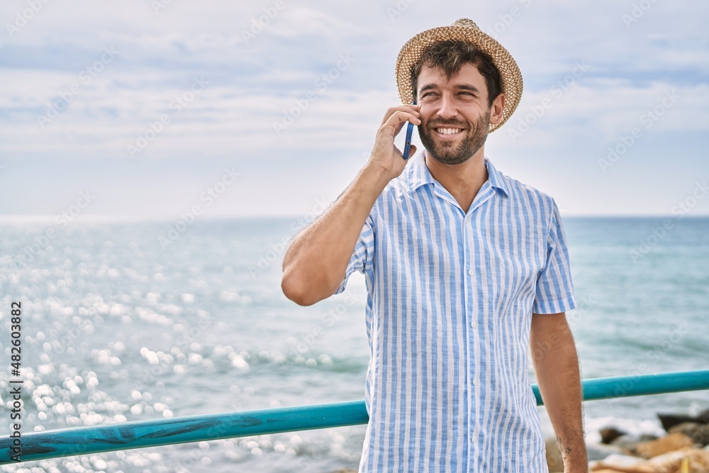Young hispanic man smiling happy talking on the smartphone at the beach