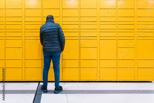 Man from behind scans a code on the mobile phone to pick up a package from the yellow locker. Messaging concept, compare online, e-commerce and packages © Davidbenito