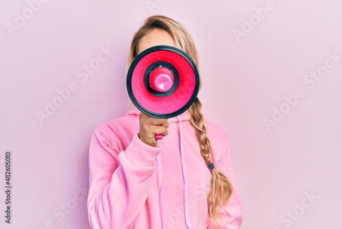 Young beautiful blonde caucasian woman shouthing and screaming through megaphone over isolated pink background