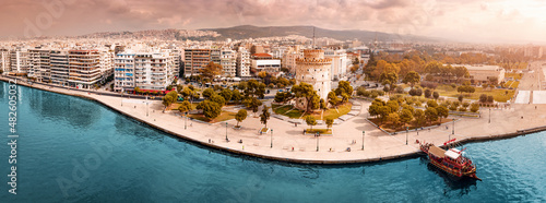 Aerial scenic panorama of the main symbol of Thessaloniki city - the White Tower with boat tour ship at the pier. Concept of travel landmarks in Greece and urban development. photo