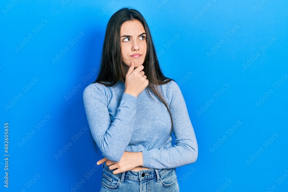 Young brunette teenager wearing casual sweater with hand on chin thinking about question, pensive expression. smiling with thoughtful face. doubt concept. Young brunette teenager wearing casual sweater with hand on chin thinking about question, pensive expression. smiling with thoughtful face. doubt concept.