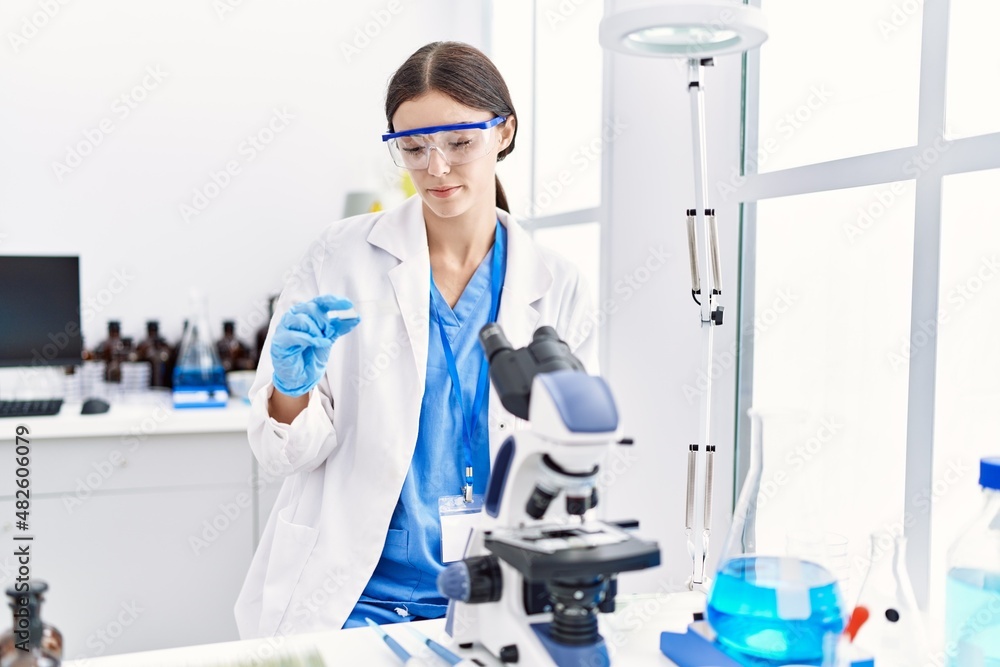 Young hispanic woman wearing scientist uniform using microscope at laboratory Young hispanic woman wearing scientist uniform using microscope at laboratory