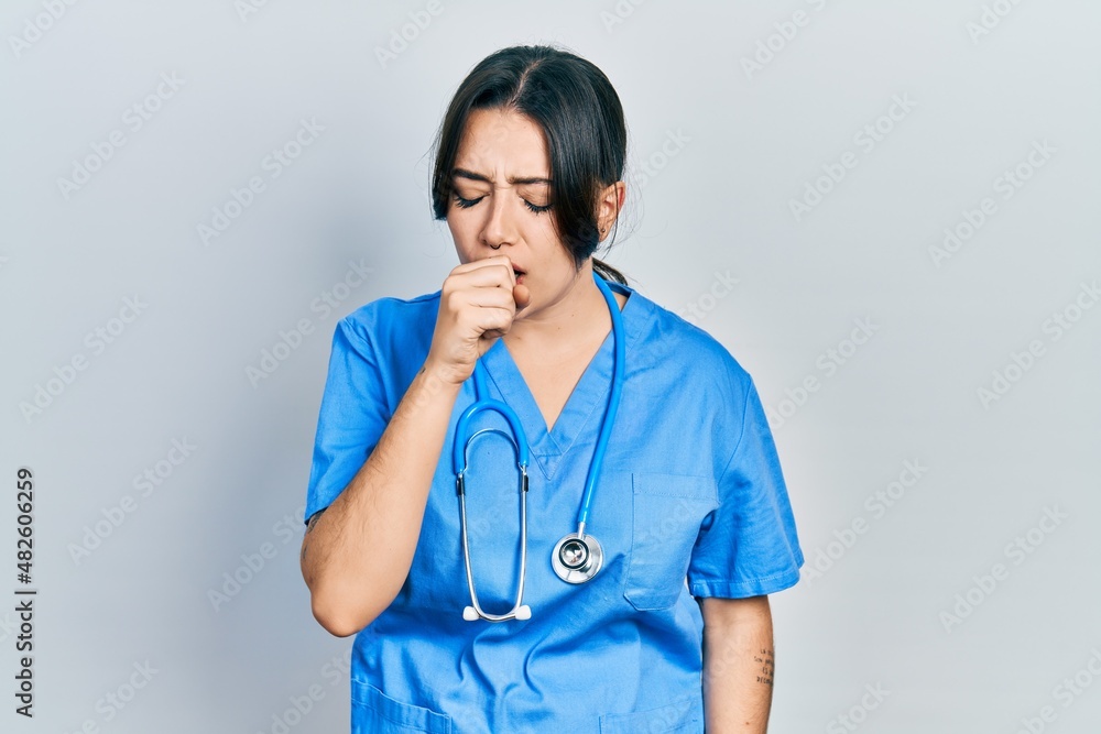 Beautiful hispanic woman wearing doctor uniform and stethoscope feeling unwell and coughing as symptom for cold or bronchitis. health care concept. Beautiful hispanic woman wearing doctor uniform and stethoscope feeling unwell and coughing as symptom for cold or bronchitis. health care concept.