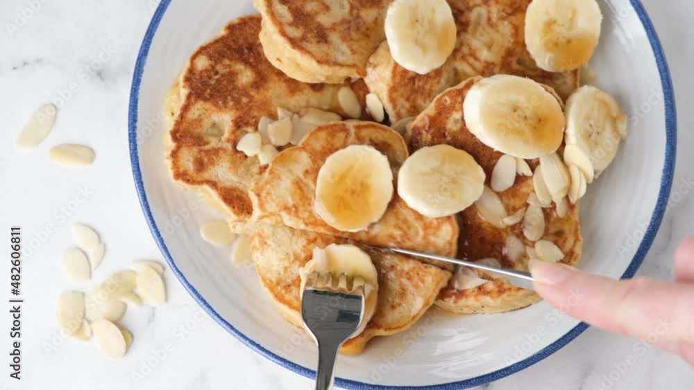 Vegan banana protein pancakes with syrup and almond flakes. Eating pancakes with fork and knife. Top view Vegan banana protein pancakes with syrup and almond flakes. Eating pancakes with fork and knife. Top view