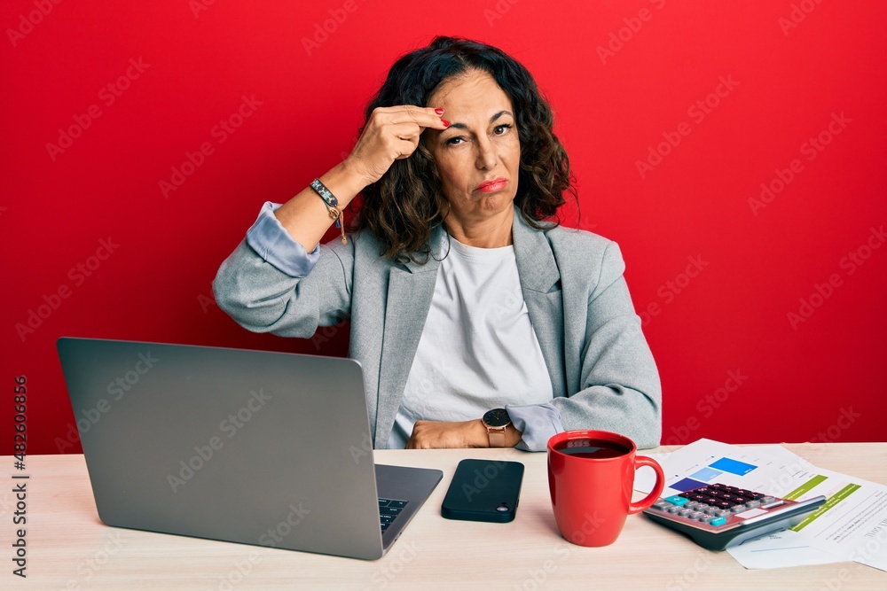 Beautiful middle age woman working at the office drinking a cup of coffee worried and stressed about a problem with hand on forehead, nervous and anxious for crisis Beautiful middle age woman working at the office drinking a cup of coffee worried and stressed about a problem with hand on forehead, nervous and anxious for crisis