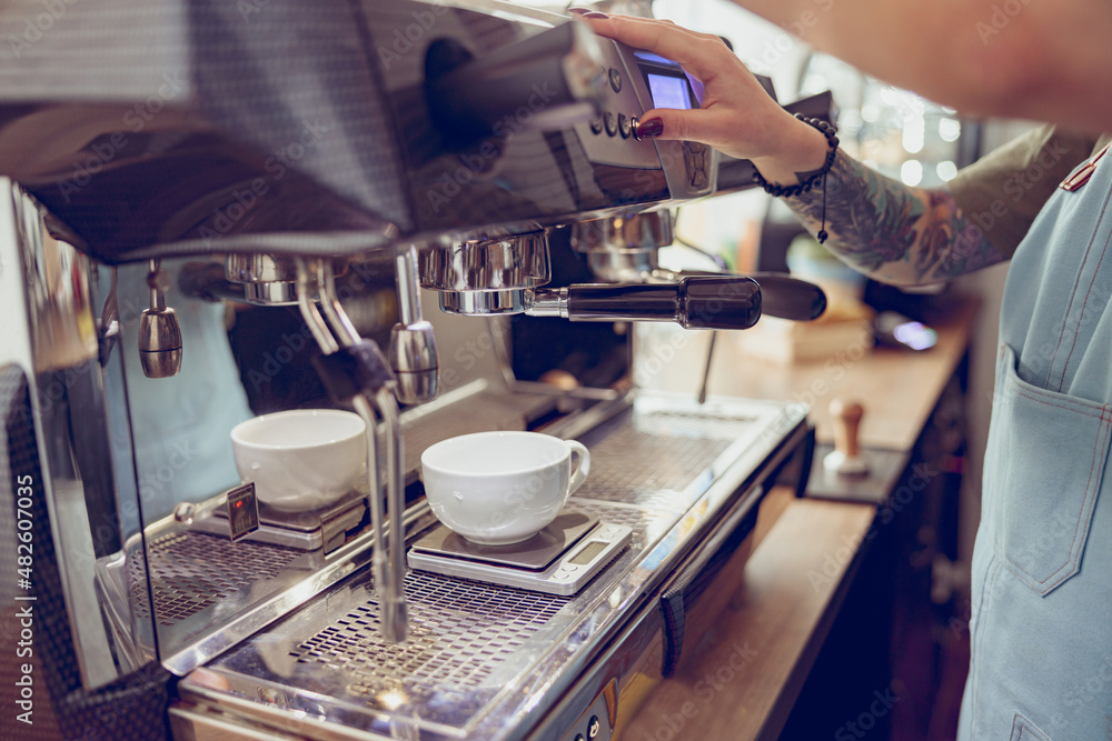 Female barista using coffee machine in cafeteria