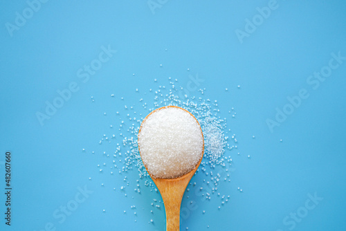 Top view of white sugar in wooden spoon on blue background with copy space