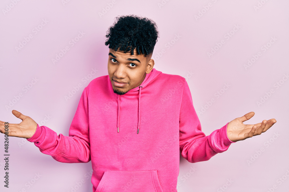 Young african american man wearing casual sweatshirt clueless and confused expression with arms and hands raised. doubt concept. Young african american man wearing casual sweatshirt clueless and confused expression with arms and hands raised. doubt concept.
