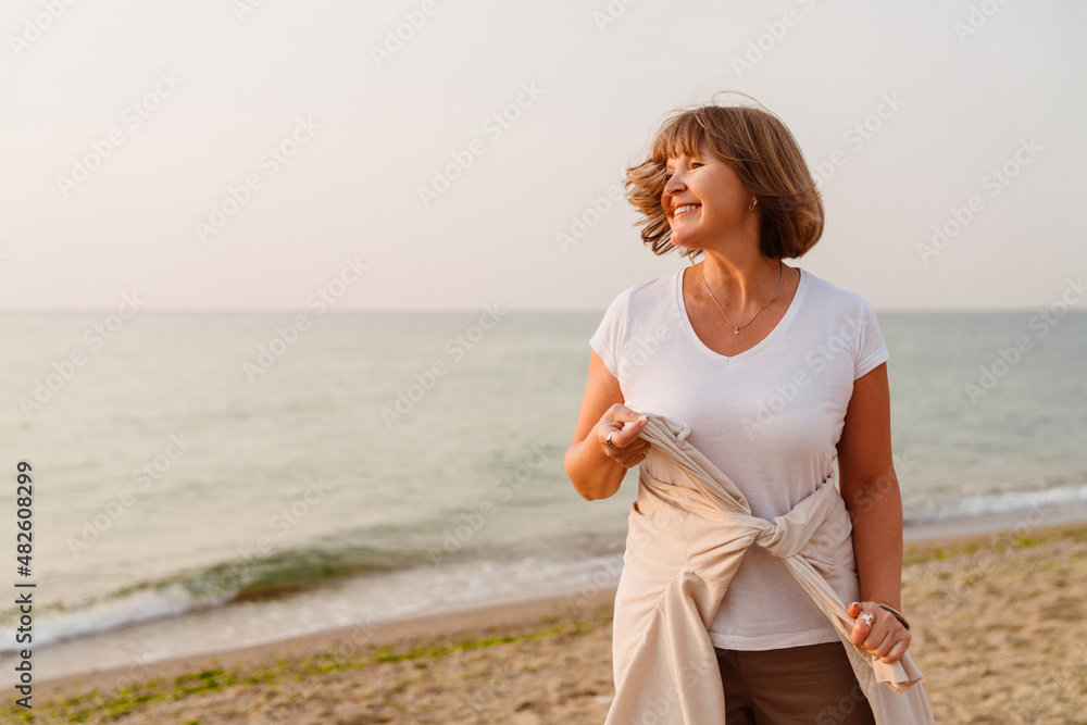 Senior european woman smiling while walking on beach