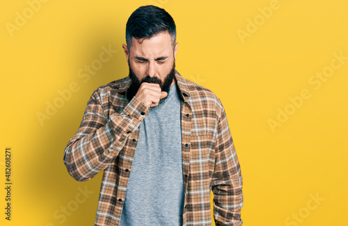 Hispanic man with beard wearing casual shirt feeling unwell and coughing as symptom for cold or bronchitis. health care concept.