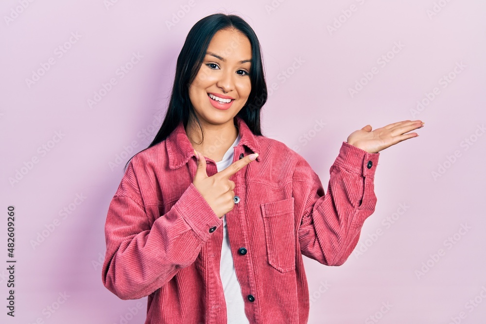 Beautiful hispanic woman with nose piercing wearing casual pink jacket amazed and smiling to the camera while presenting with hand and pointing with finger. Beautiful hispanic woman with nose piercing wearing casual pink jacket amazed and smiling to the camera while presenting with hand and pointing with finger.