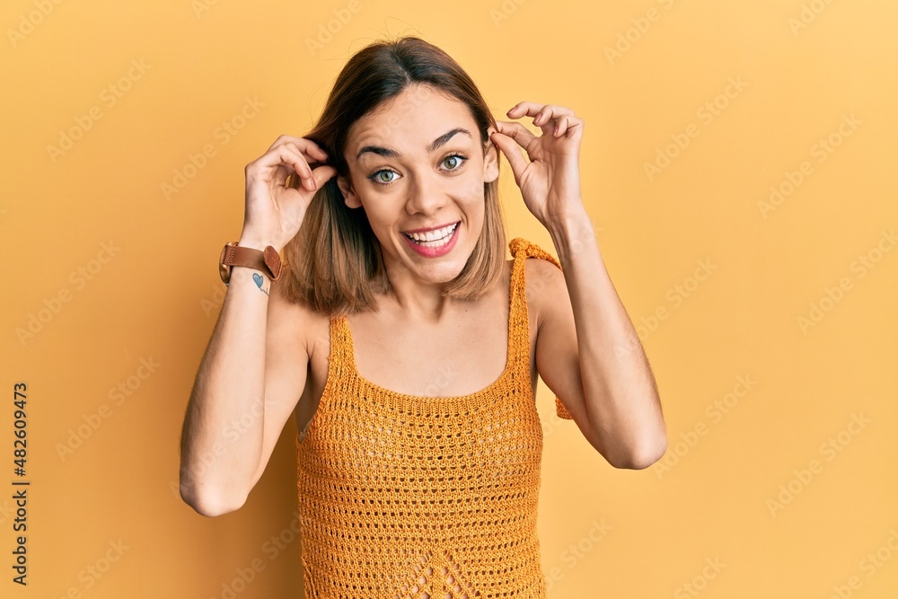 Young caucasian blonde woman wearing casual yellow t shirt smiling pulling ears with fingers, funny gesture. audition problem Young caucasian blonde woman wearing casual yellow t shirt smiling pulling ears with fingers, funny gesture. audition problem