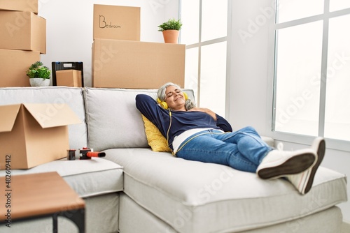 Middle age grey-haired woman listening to music lying on the sofa at new home.