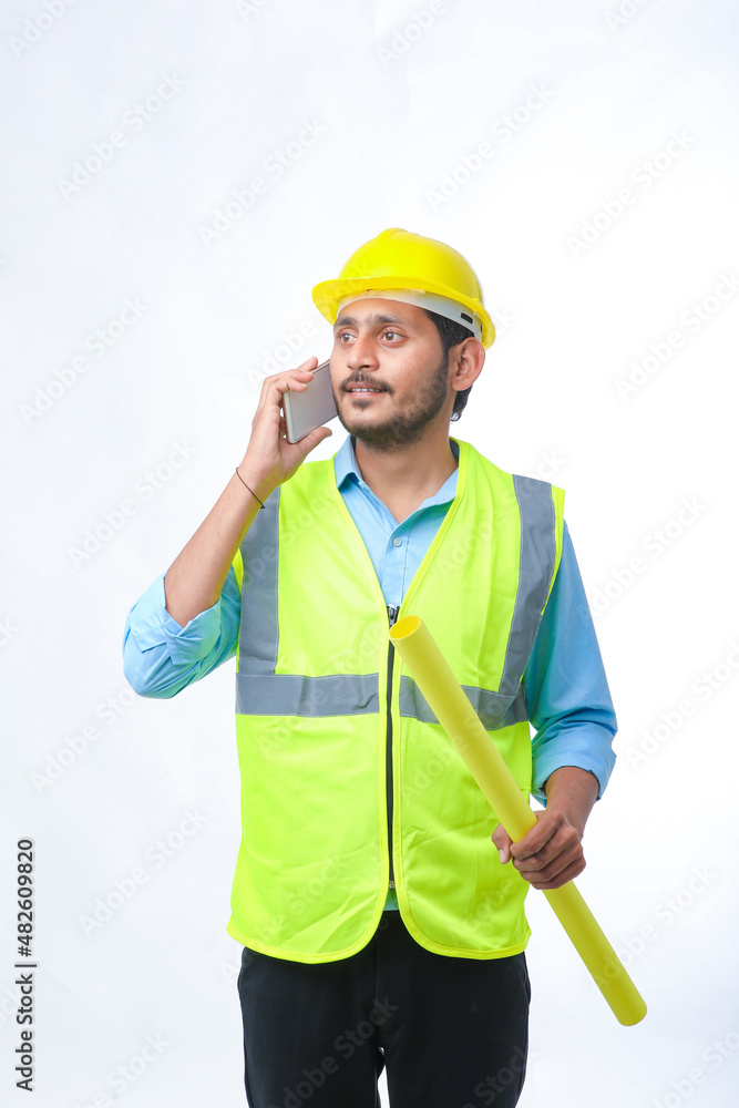 Young indian engineer wearing hardhat and talking smartphone on white background. Young indian engineer wearing hardhat and talking smartphone on white background.