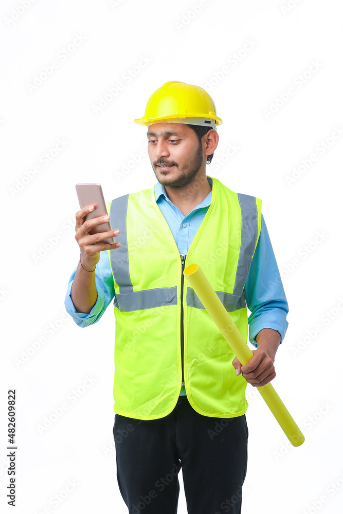 Young indian engineer wearing hardhat and using smartphone on white background. Young indian engineer wearing hardhat and using smartphone on white background.