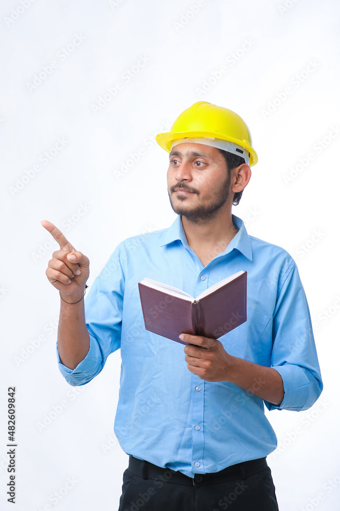 Young indian engineer wearing hardhat and watching diary Young indian engineer wearing hardhat and watching diary