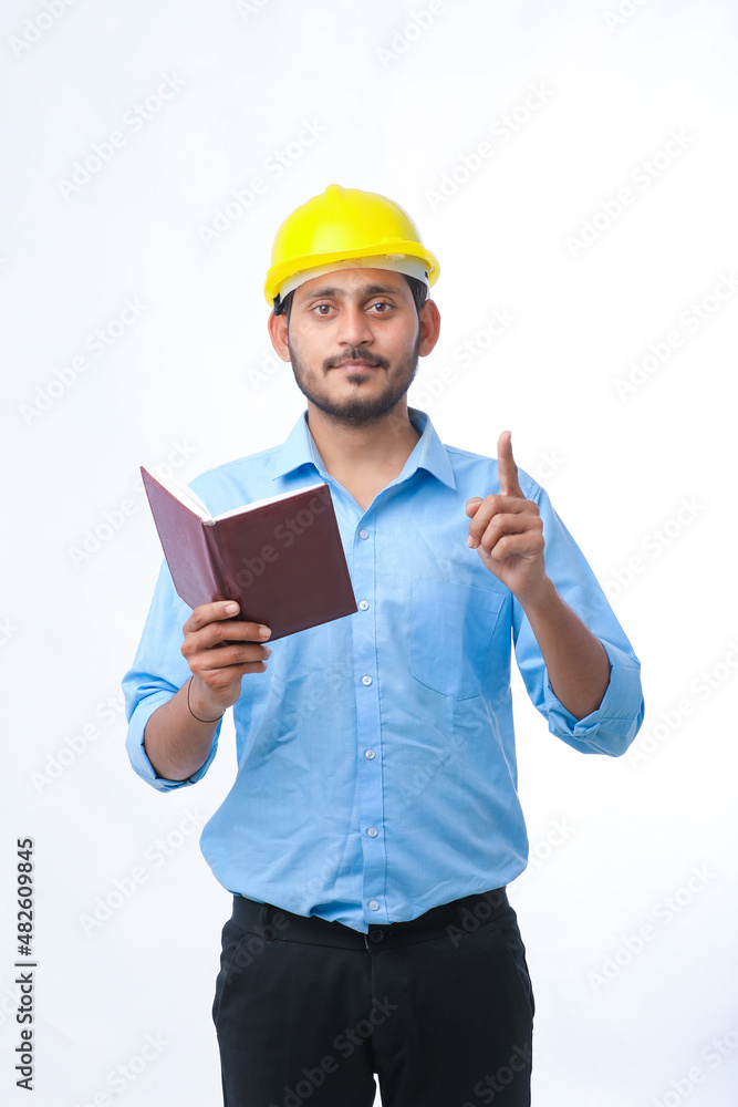 Young indian engineer wearing hardhat and watching diary Young indian engineer wearing hardhat and watching diary