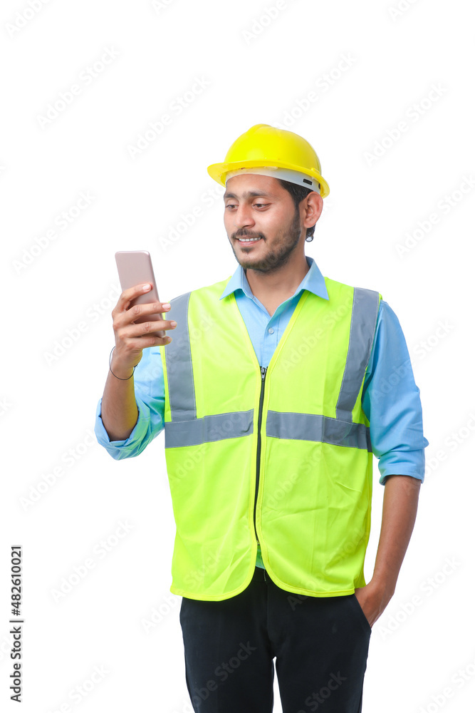 Young indian engineer wearing hardhat and using smartphone on white background. Young indian engineer wearing hardhat and using smartphone on white background.