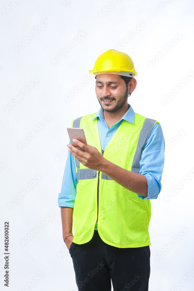 Young indian engineer wearing hardhat and using smartphone on white background. Young indian engineer wearing hardhat and using smartphone on white background.