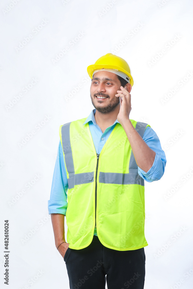 Young indian engineer wearing hardhat and talking smartphone on white background. Young indian engineer wearing hardhat and talking smartphone on white background.