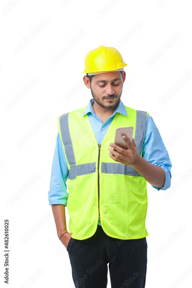 Young indian engineer wearing hardhat and using smartphone on white background. Young indian engineer wearing hardhat and using smartphone on white background.