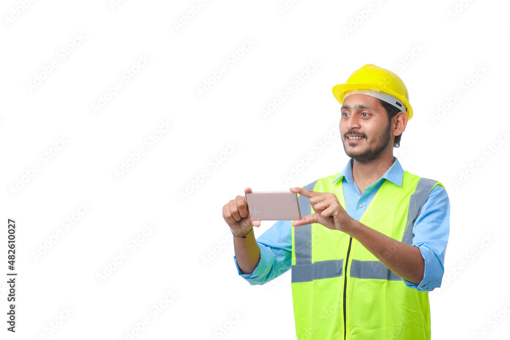 Young indian engineer wearing hardhat and using smartphone on white background. Young indian engineer wearing hardhat and using smartphone on white background.