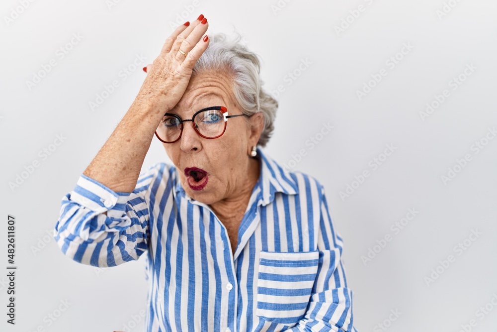 Senior woman with grey hair standing over white background surprised with hand on head for mistake, remember error. forgot, bad memory concept. - obrazy, fototapety, plakaty 