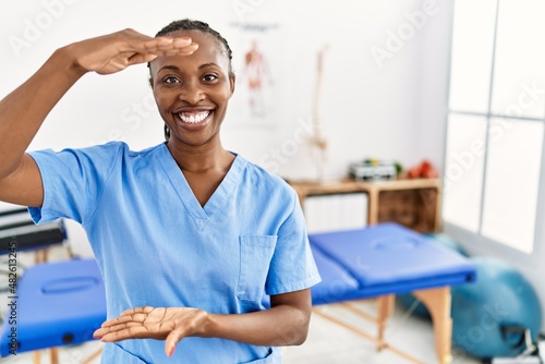 Black woman with braids working at pain recovery clinic gesturing with hands showing big and large size sign, measure symbol. smiling looking at the camera. measuring concept.