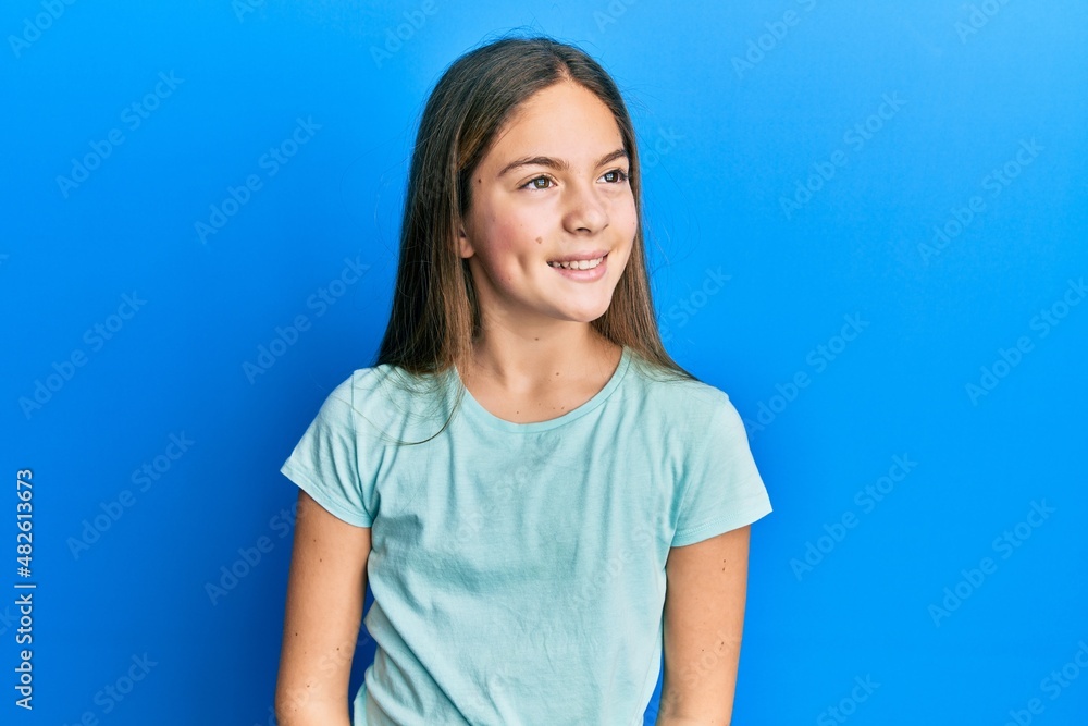 Beautiful brunette little girl wearing casual white t shirt looking away to side with smile on face, natural expression. laughing confident. Beautiful brunette little girl wearing casual white t shirt looking away to side with smile on face, natural expression. laughing confident.