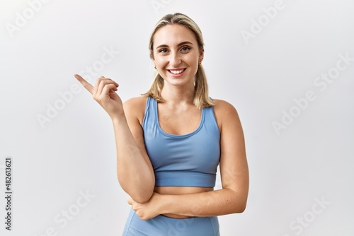 Young blonde woman wearing sportswear over isolated background smiling happy pointing with hand and finger to the side