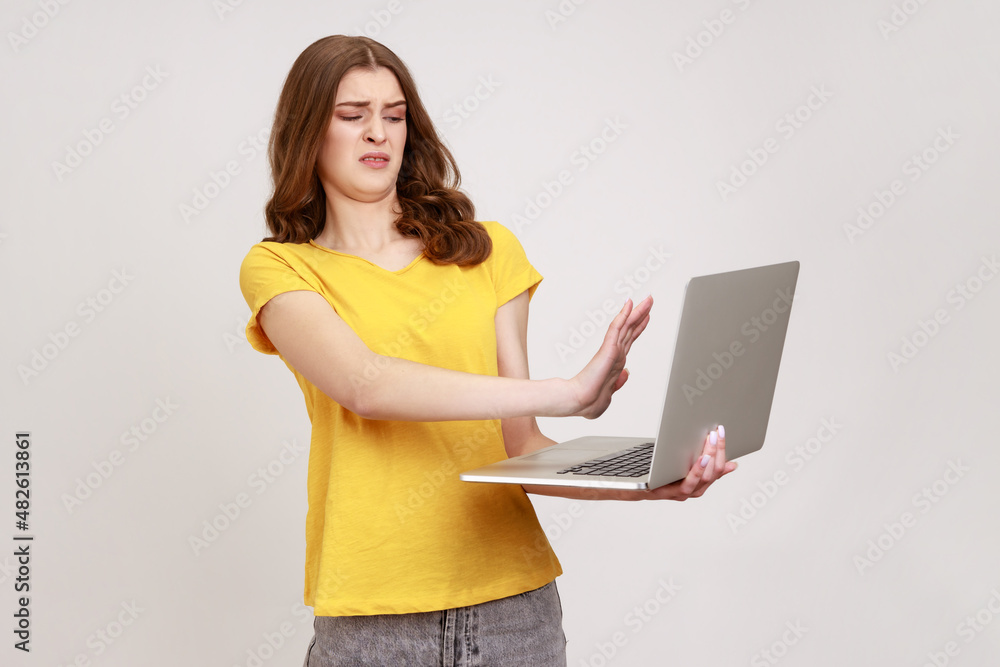 Forbidden content. Frightened teenager girl closing laptop and keeping hand in stop gesture to cover shameful post on internet, troubles with computer. Indoor studio shot isolated on gray background. Forbidden content. Frightened teenager girl closing laptop and keeping hand in stop gesture to cover shameful post on internet, troubles with computer. Indoor studio shot isolated on gray background.