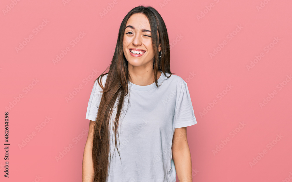 Young hispanic girl wearing casual white t shirt winking looking at the camera with sexy expression, cheerful and happy face. Young hispanic girl wearing casual white t shirt winking looking at the camera with sexy expression, cheerful and happy face.