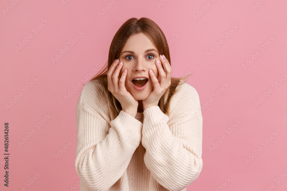 Portrait of positive blond woman looking nat camera with excitement, keeping hands on cheeks, pleasant surprise, wearing white sweater. Indoor studio shot isolated on pink background. Portrait of positive blond woman looking nat camera with excitement, keeping hands on cheeks, pleasant surprise, wearing white sweater. Indoor studio shot isolated on pink background.