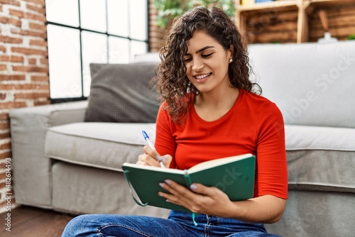 Young latin woman smiling confident writing on book at home