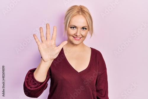 Young blonde woman wearing casual winter sweater showing and pointing up with fingers number five while smiling confident and happy.
