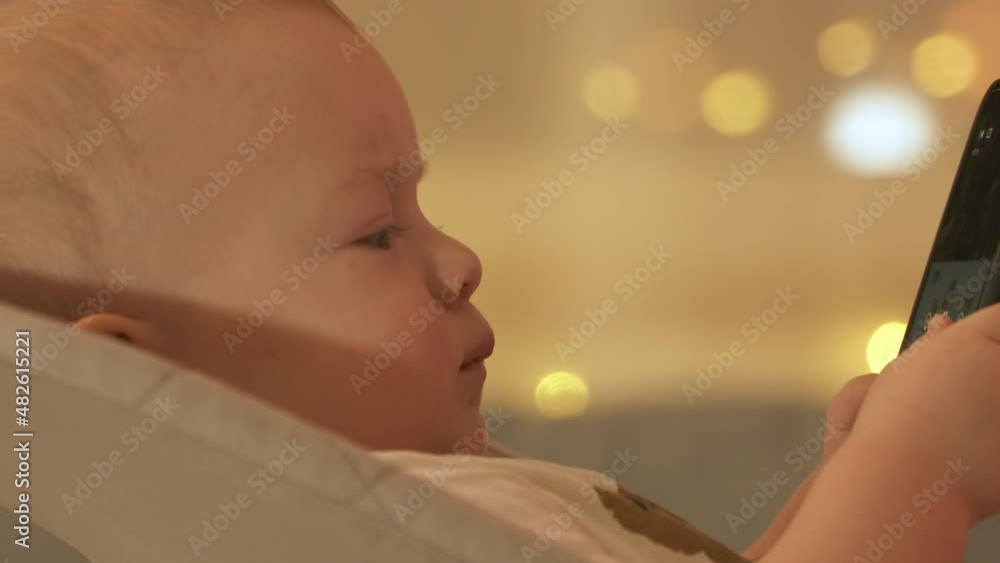 Cute toddler boy sitting on rocking chair in living room and watching something on mobile phone screen, 9 months old caucasian baby using smartphone at home. High quality 4k footage Cute toddler boy sitting on rocking chair in living room and watching something on mobile phone screen, 9 months old caucasian baby using smartphone at home. High quality 4k footage