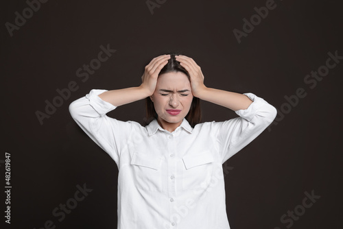 Young woman suffering from headache on brown background