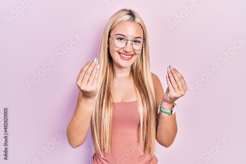 Young blonde girl wearing casual clothes doing money gesture with hands, asking for salary payment, millionaire business