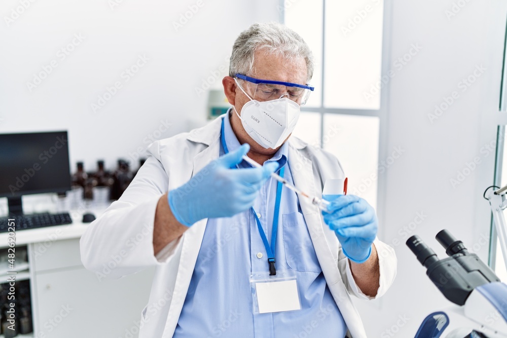 Middle age grey-haired man wearing scientist uniform using syringe at laboratory Middle age grey-haired man wearing scientist uniform using syringe at laboratory