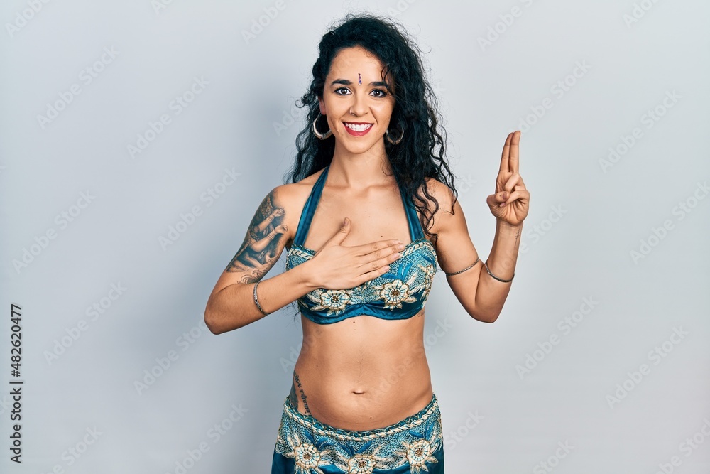Fototapeta premium Young woman wearing bindi and traditional belly dance clothes smiling swearing with hand on chest and fingers up, making a loyalty promise oath