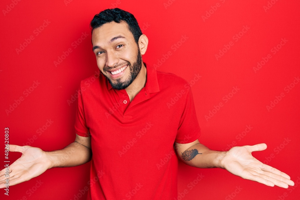 Hispanic man with beard wearing casual red t shirt clueless and confused expression with arms and hands raised. doubt concept. Hispanic man with beard wearing casual red t shirt clueless and confused expression with arms and hands raised. doubt concept.